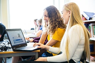 To smilende elever som jobber sammen på en bærbar PC i et klasserom