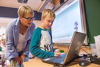 Lærer og elev ser på en bærbar PC mens en quiz vises på storskjermen