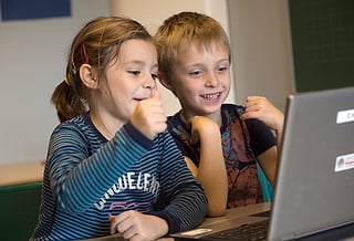 En jente og en gutt smiler til en bærbar PC-skjerm og gir tommelen opp